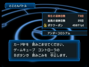 The menu displayed in between battles in Endless Battle mode. A blue title card in the top left displays Endless Battle in Japanese. Two grey fields extend from the middle right displaying the current win streak at 73 and the record win streak at 25, with 45,971 Poké Coupons. The field below displays Under Colosseum in Japanese. A text box centered towards the bottom reads in Japanese "Scan a Pokémon Colosseum Double Battle e+ card. Press B to cancel." The background is a glowing outline of a stadium with a Poke Ball design in the center.